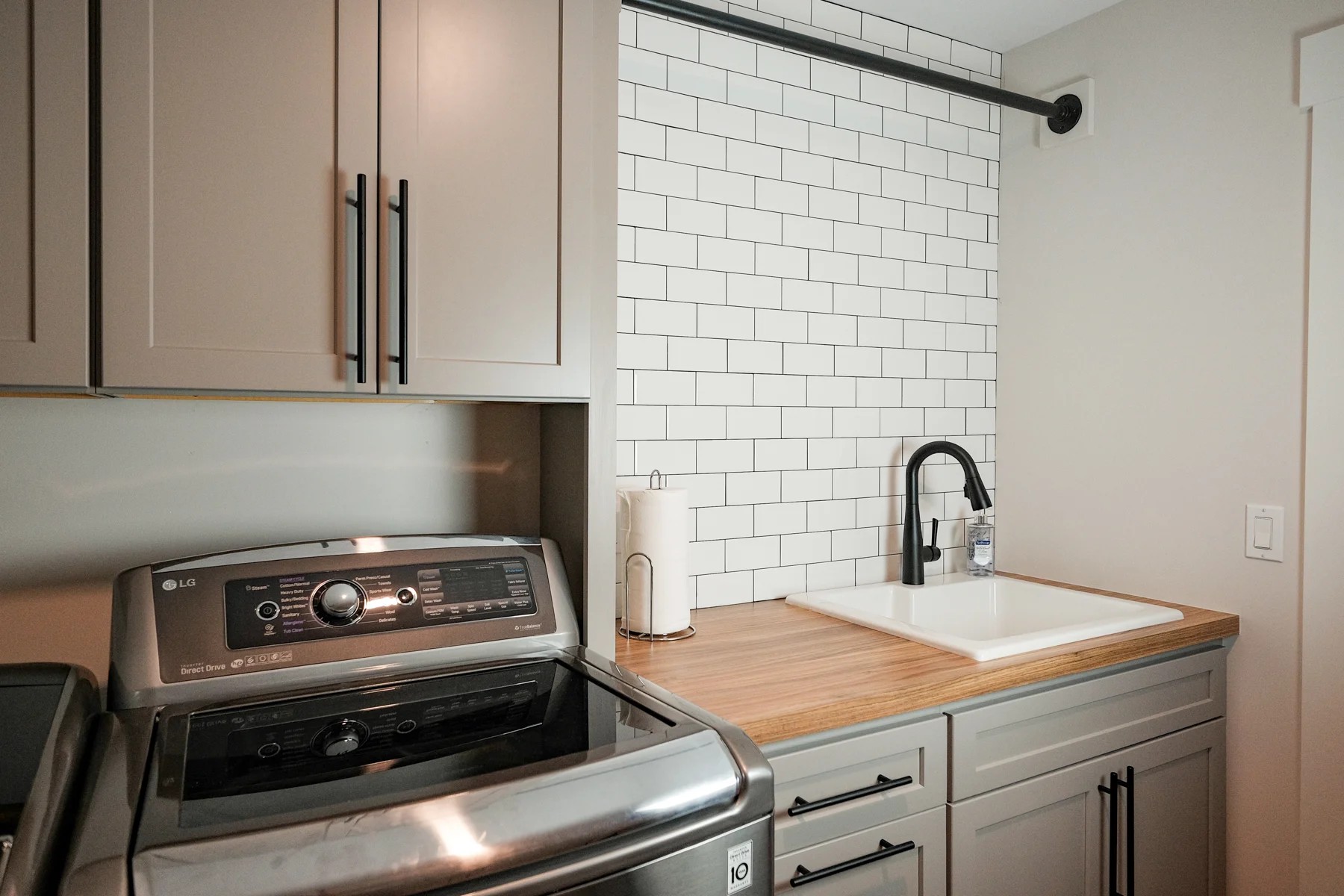 A laundry room with white subway tile, a butcher-block counter, a top-load washer, and a black faucet.