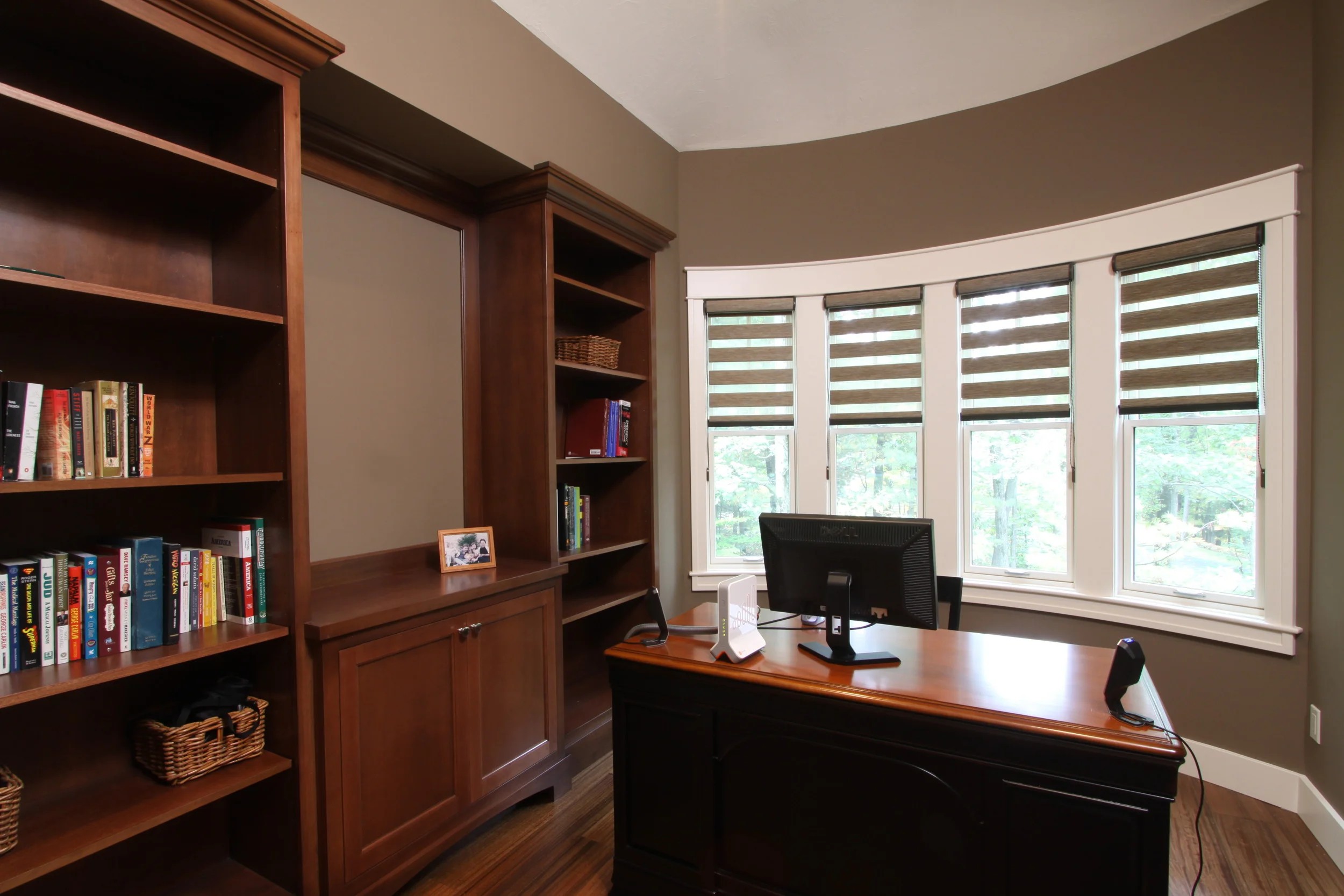 A home office and library with cherry built-in bookcases wrapping a curved bay window.