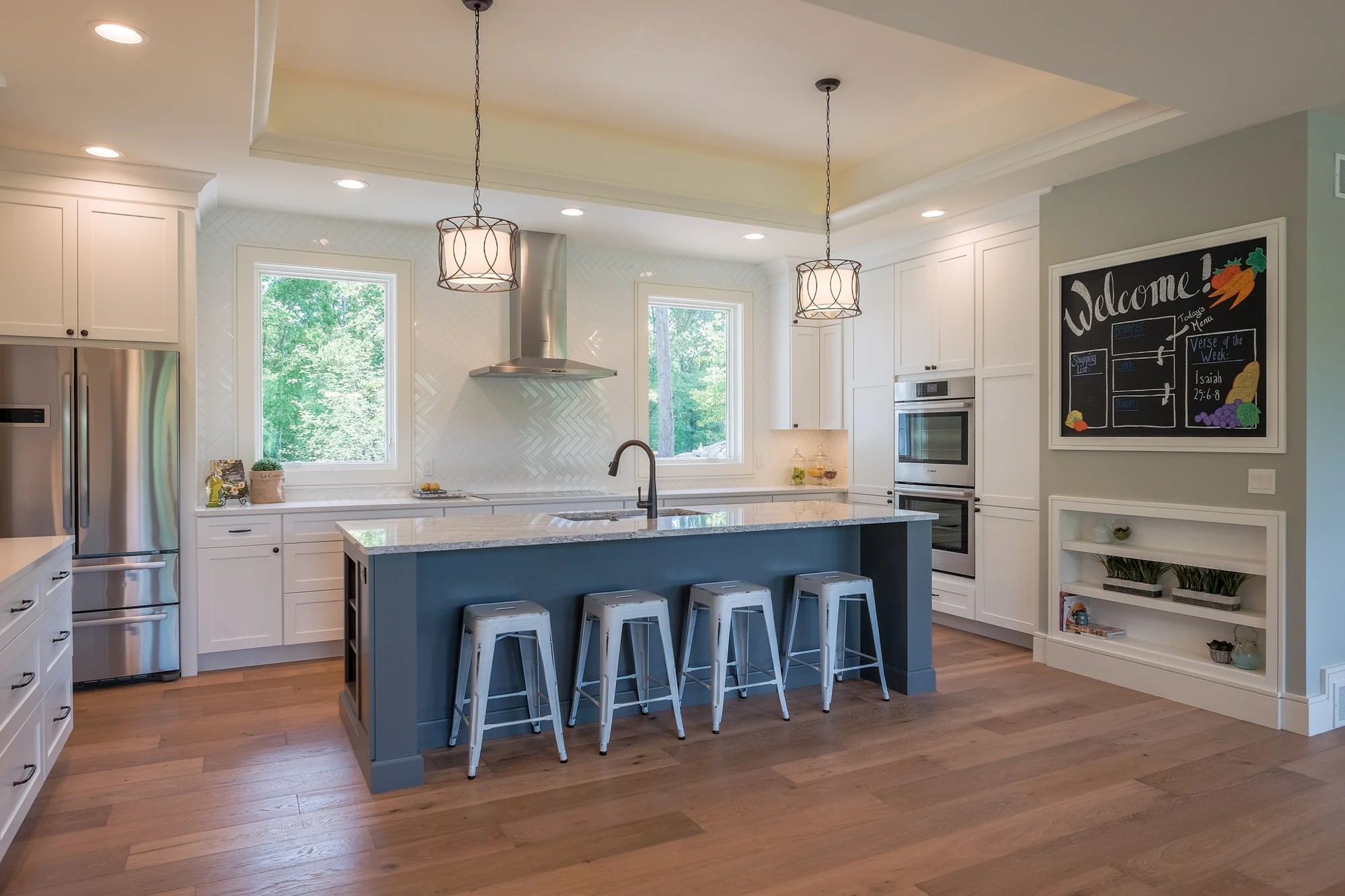 Kitchen with white shaker cabinets, a navy-blue island with marble countertops, herringbone backsplash, and pendant lights over metal stools.