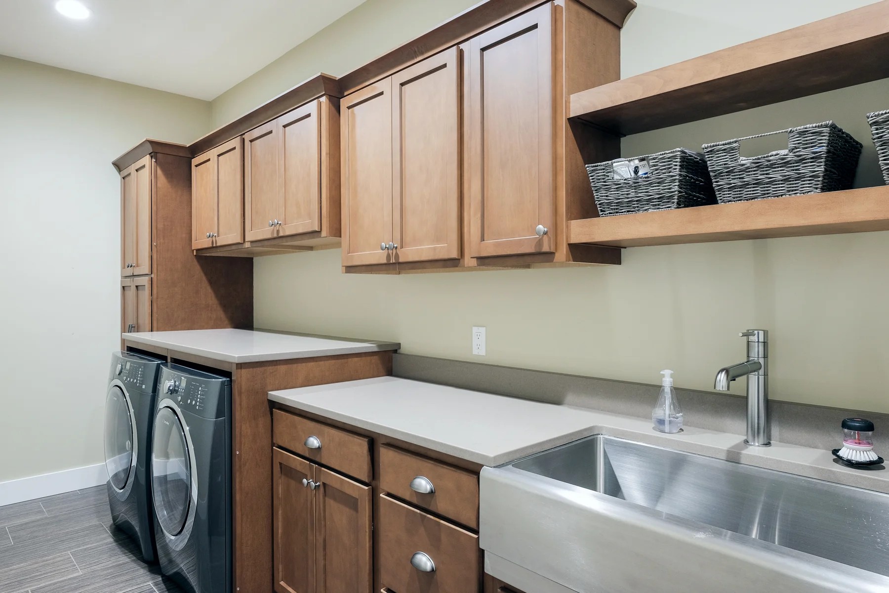 A laundry and mudroom with maple cabinets, a stainless apron-front sink, and open shelving with baskets.