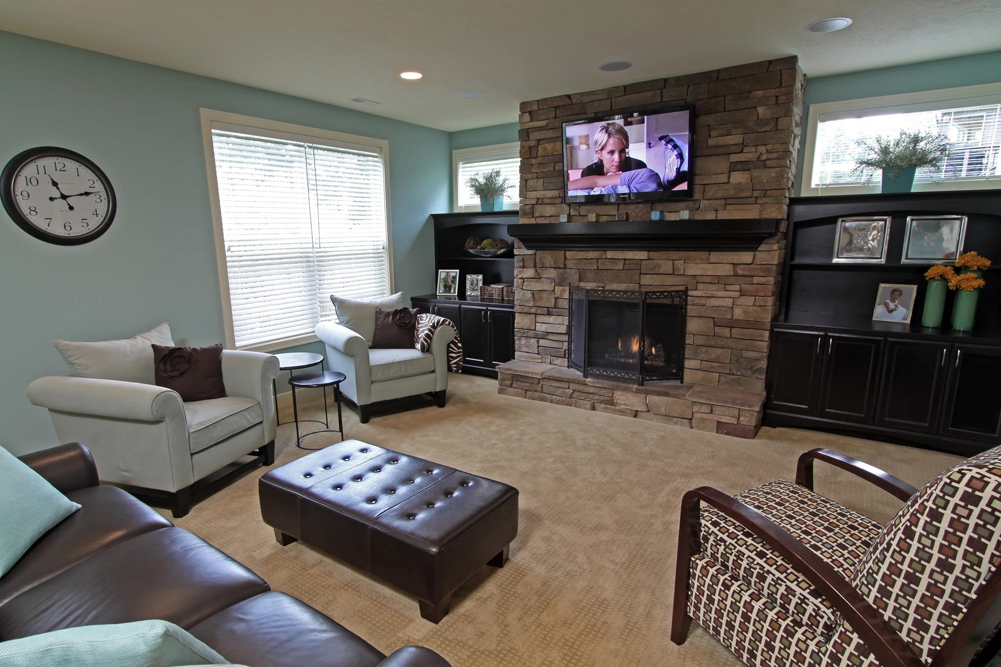 A lower-level family room with a stacked-stone fireplace, dark built-ins, teal walls, and a leather sofa.